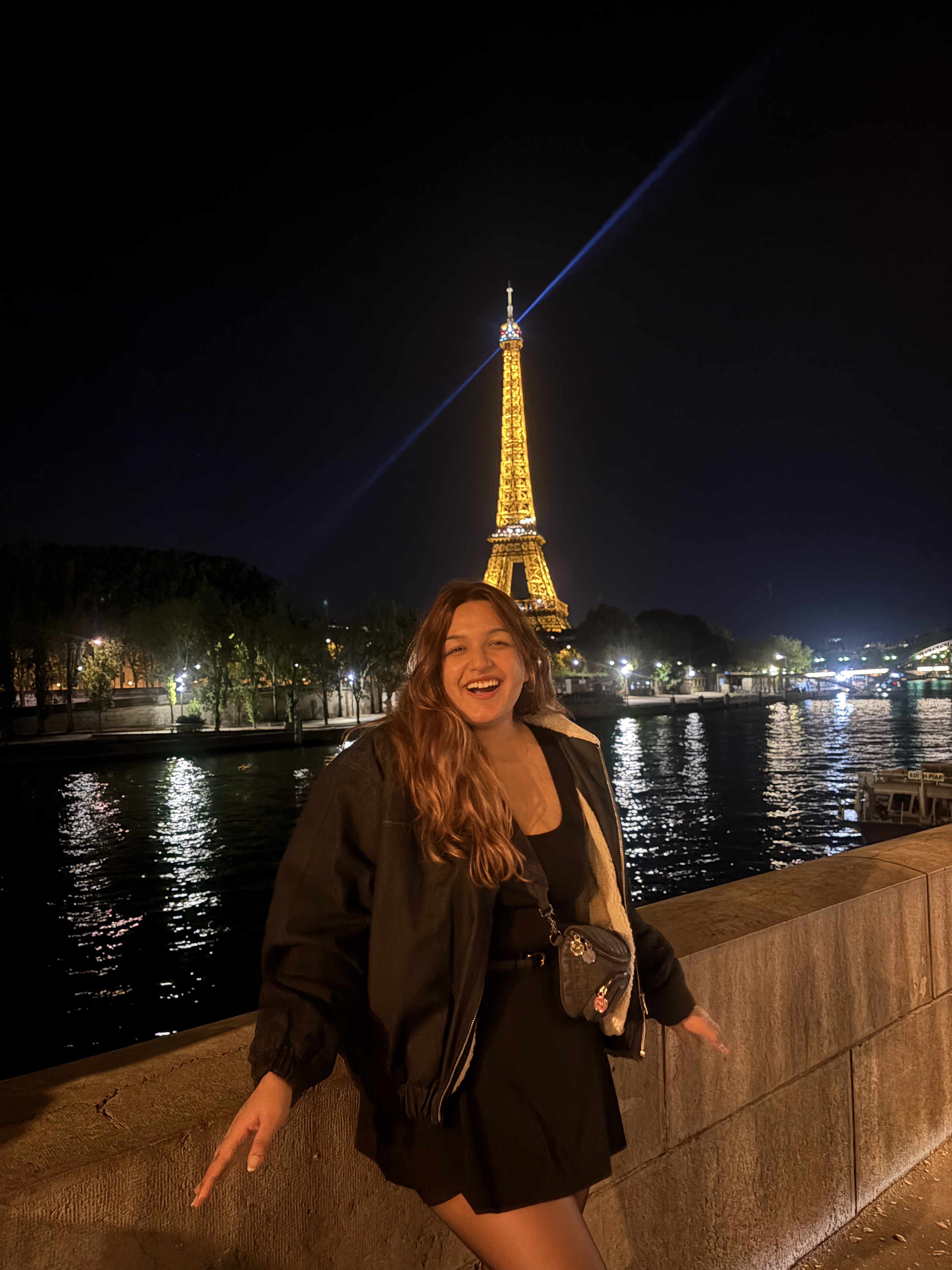 Falguni Mahajan smiling in front of the illuminated Eiffel Tower in Paris at night